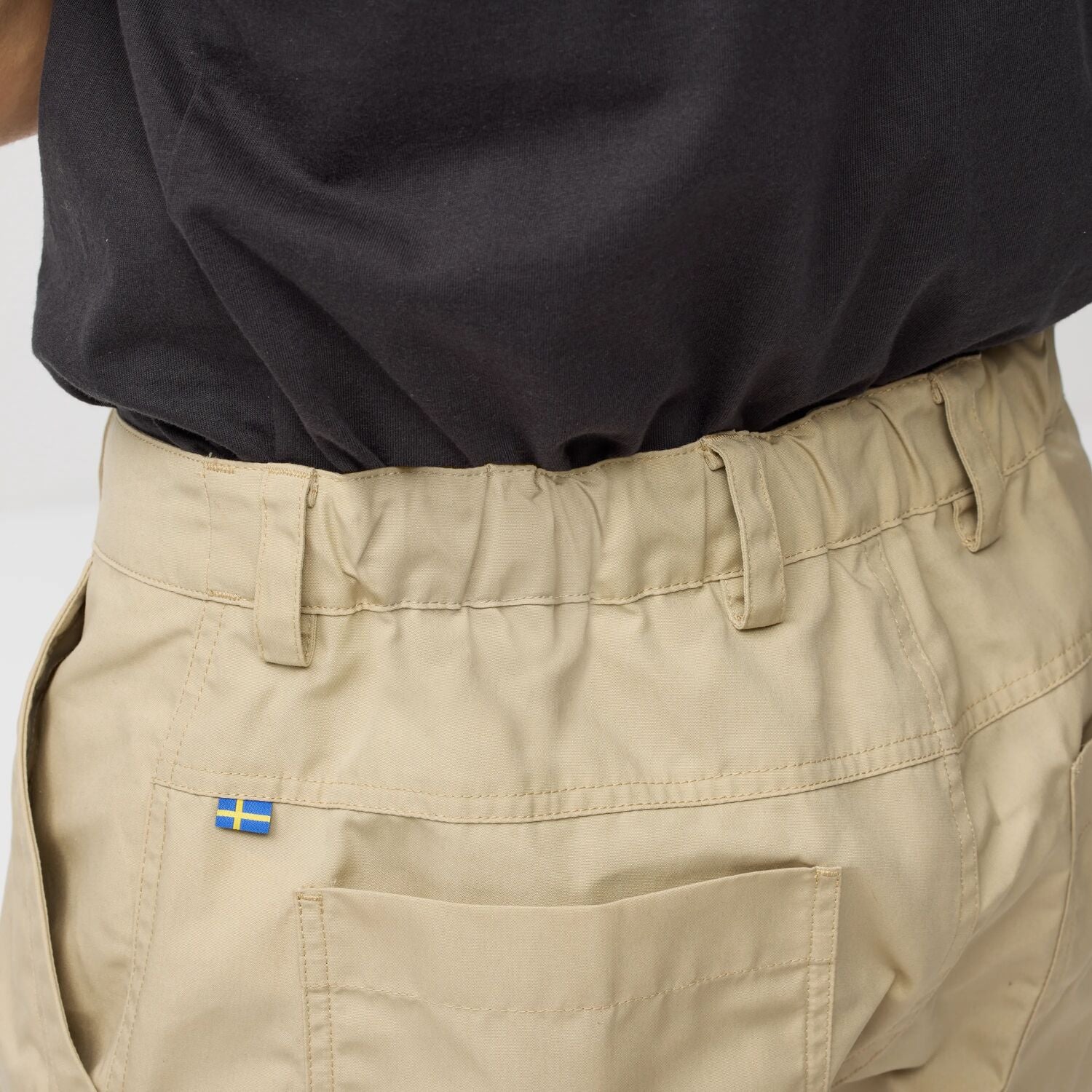 Beige pants with a sweden flag logo on the pocket against a neutral background