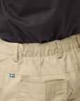 Beige pants with a sweden flag logo on the pocket against a neutral background