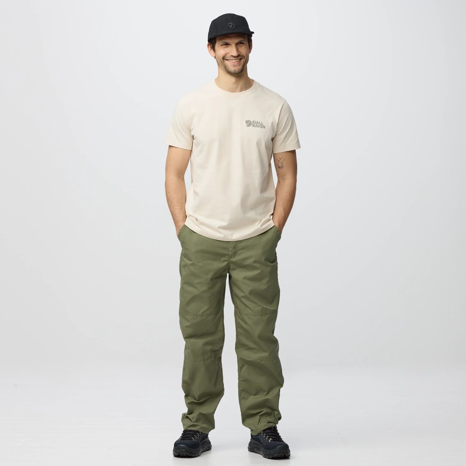 Man wearing a beige t-shirt and green pants on a white background