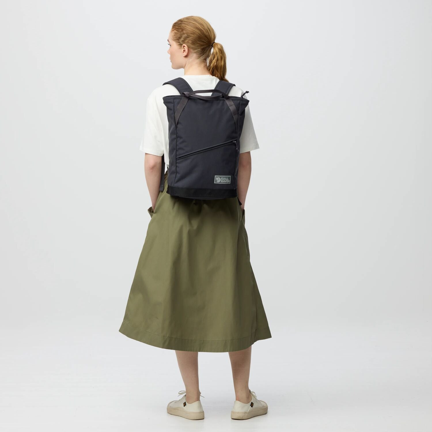 Person wearing a black backpack and green skirt on a white background