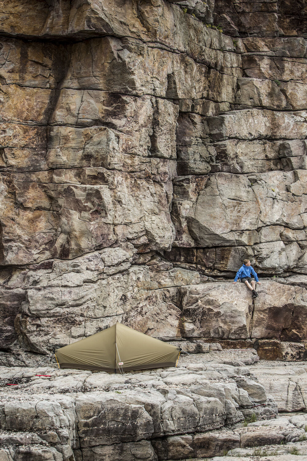 Person climbing a rocky cliff with a tent below.