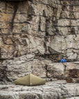 Person climbing a rocky cliff with a tent below.