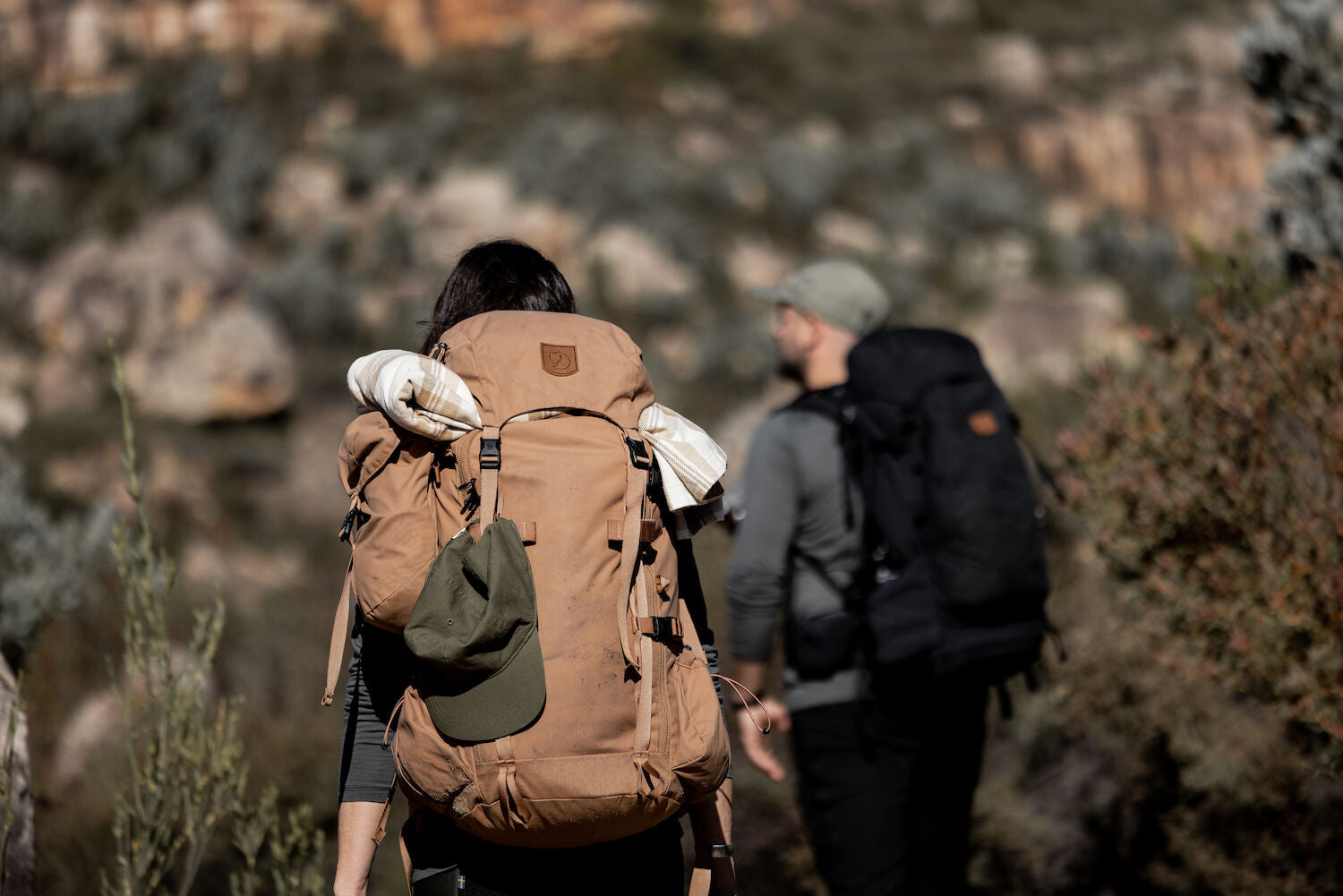 Two hikers with backpacks walking through a rocky landscape.