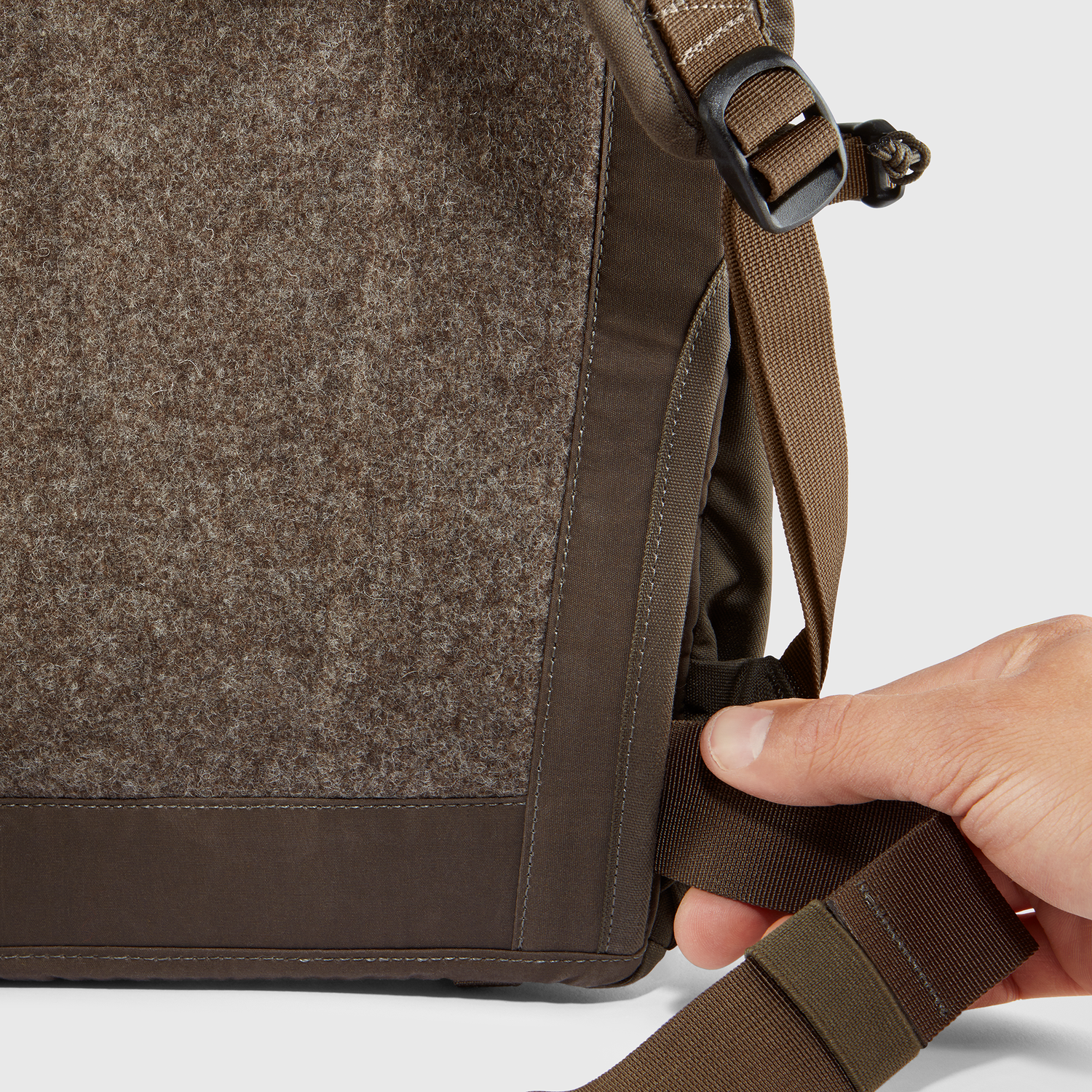 Close-up of a brown backpack with a hand adjusting the strap on a white background