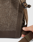 Close-up of a brown backpack with a hand adjusting the strap on a white background