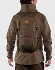 Person wearing a brown jacket and backpack on a light gray background