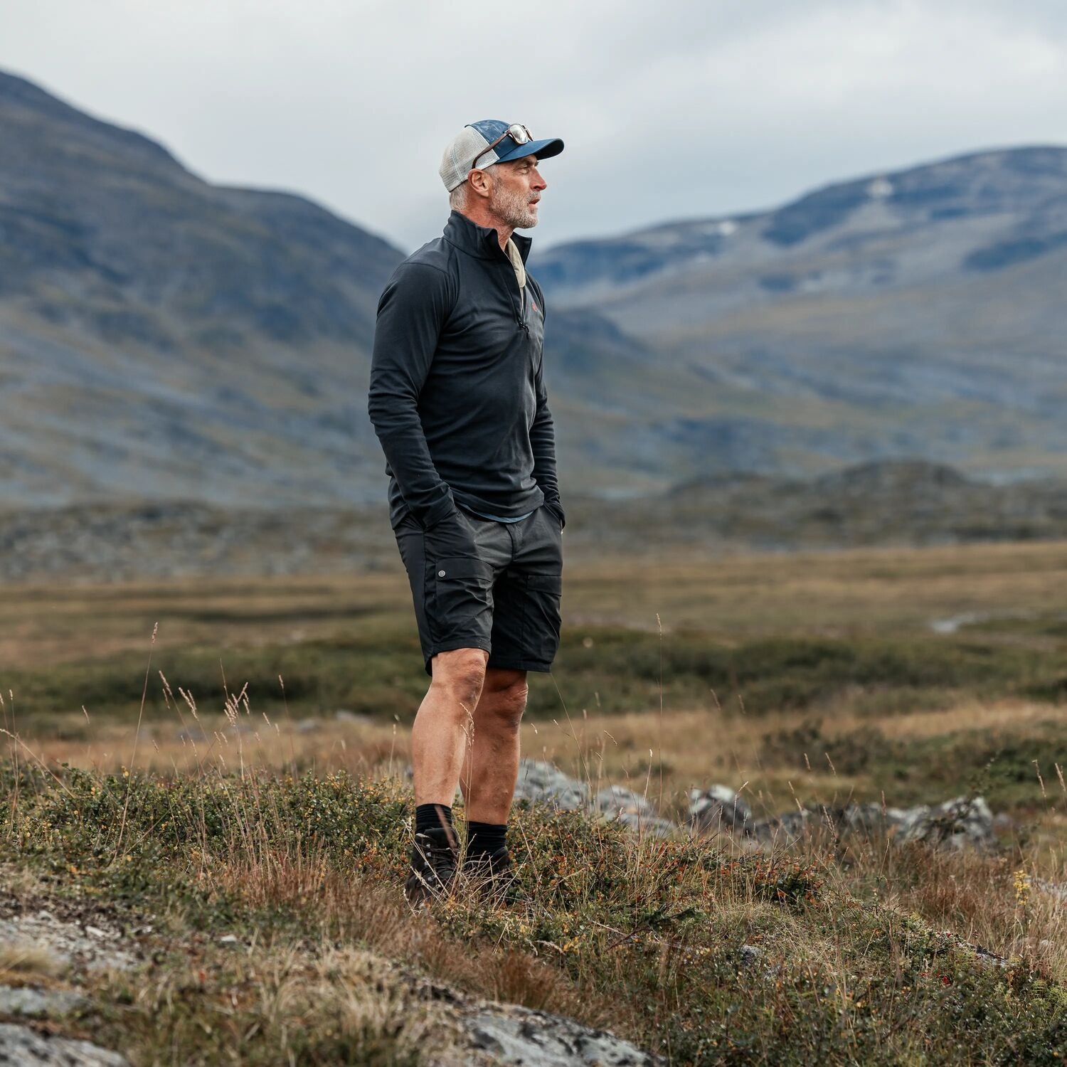 Man standing in a mountainous landscape wearing athletic gear.