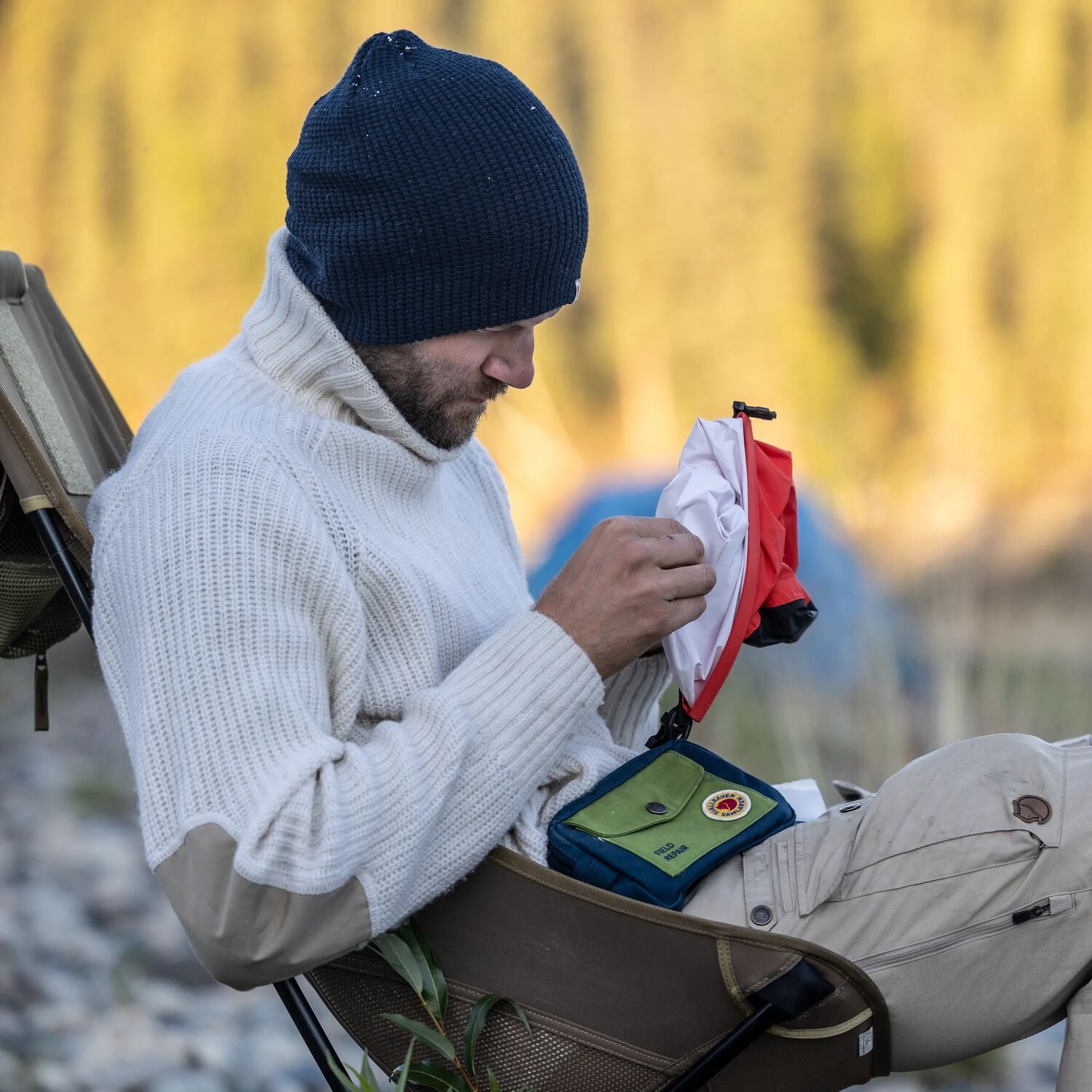 Man sitting outdoors in a natural setting, organizing items in a bag.