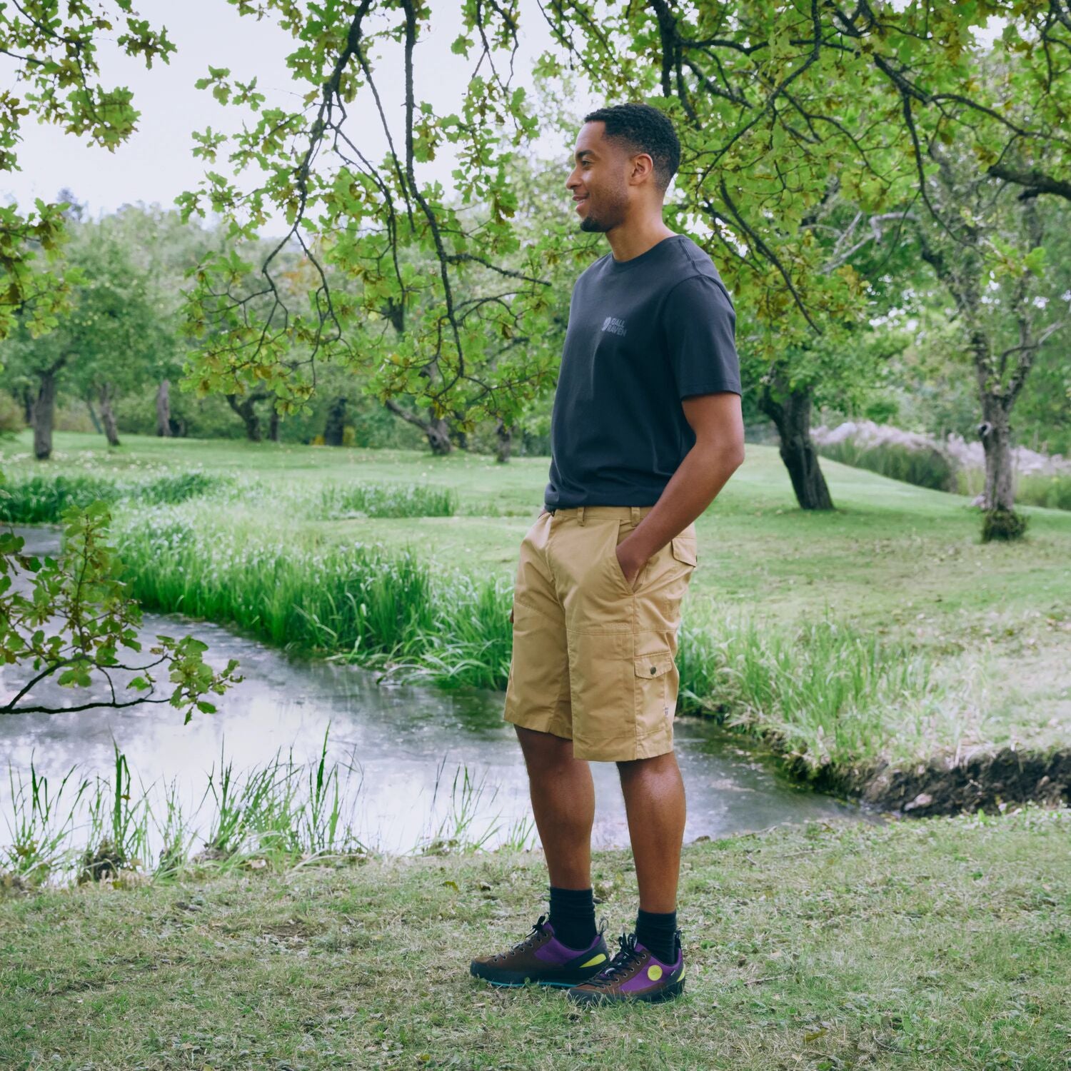 Man standing in a park by a stream with trees and grass in the background