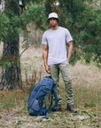 Man standing in a forest with a blue backpack
