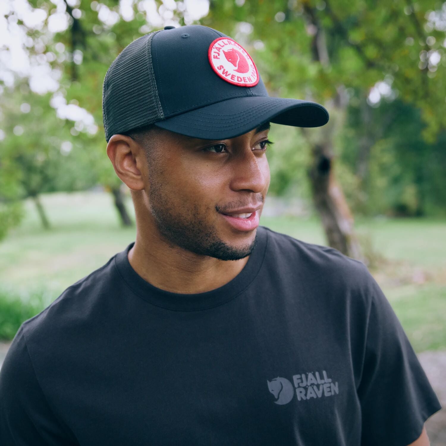 Man wearing a black cap and black t-shirt with Fjällräven logo outdoors
