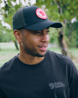 Man wearing a black cap and black t-shirt with Fjällräven logo outdoors