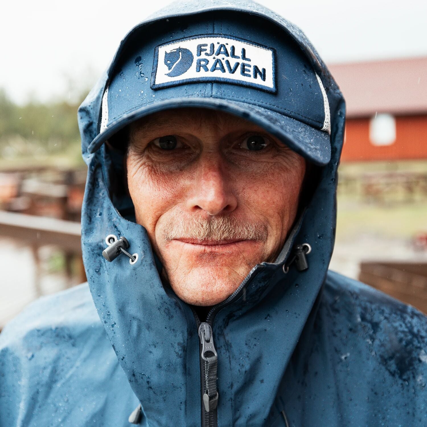 Person wearing a blue raincoat and cap with Fjällräven logo outdoors.