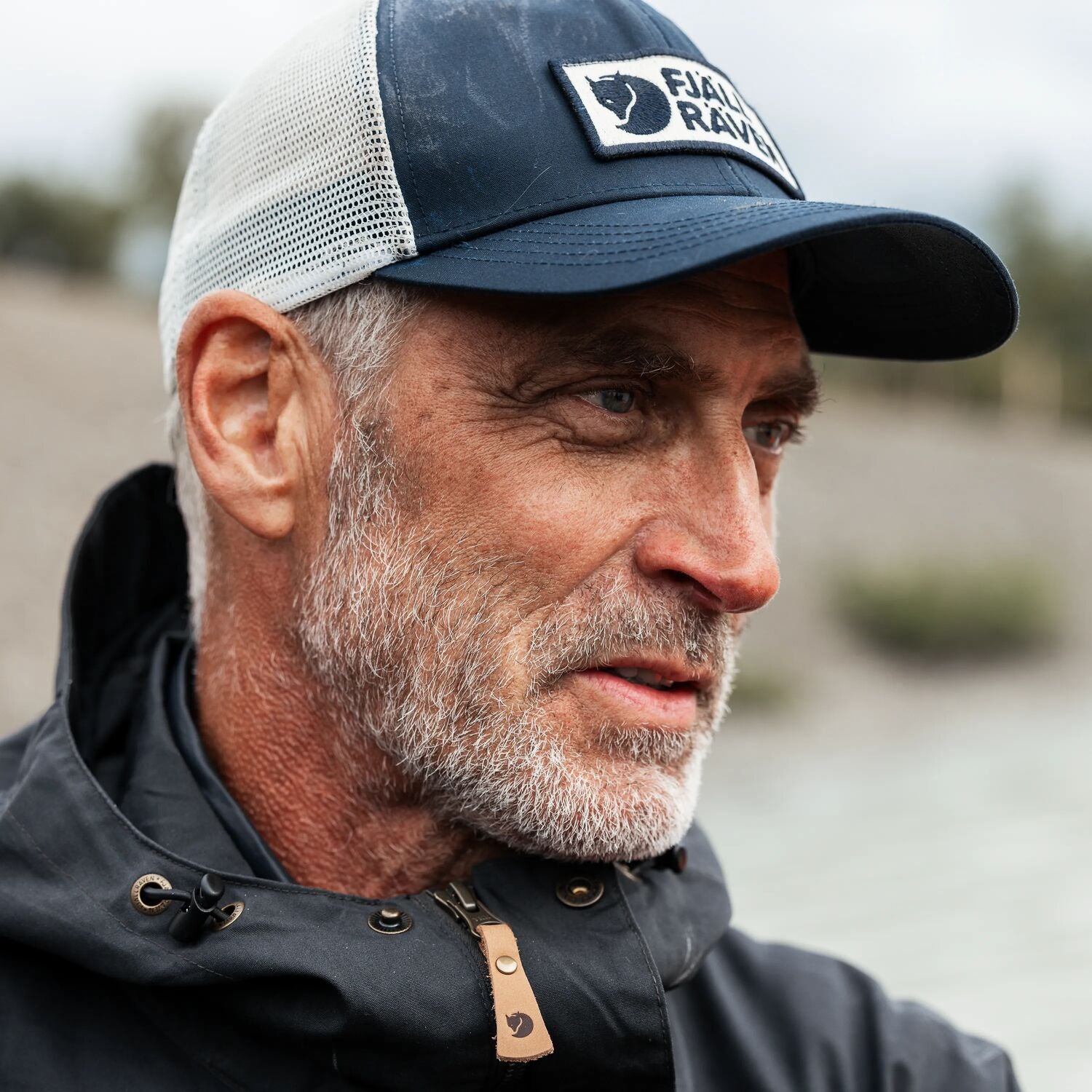Man wearing a cap with a Fjällräven logo outdoors