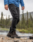 Person in outdoor setting wearing a blue jacket and black pants with hiking boots near a campfire.