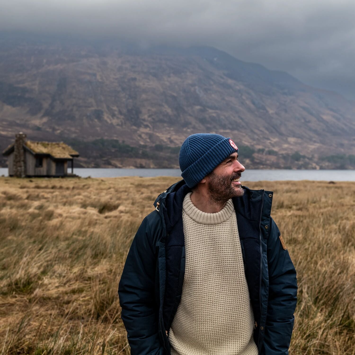 Man standing in a field with mountains and a lake in the background