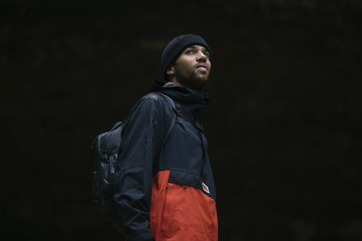 man wearing black-orange raincoat jacket with Fjällräven logo and a black beanie