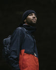man wearing black-orange raincoat jacket with Fjällräven logo and a black beanie