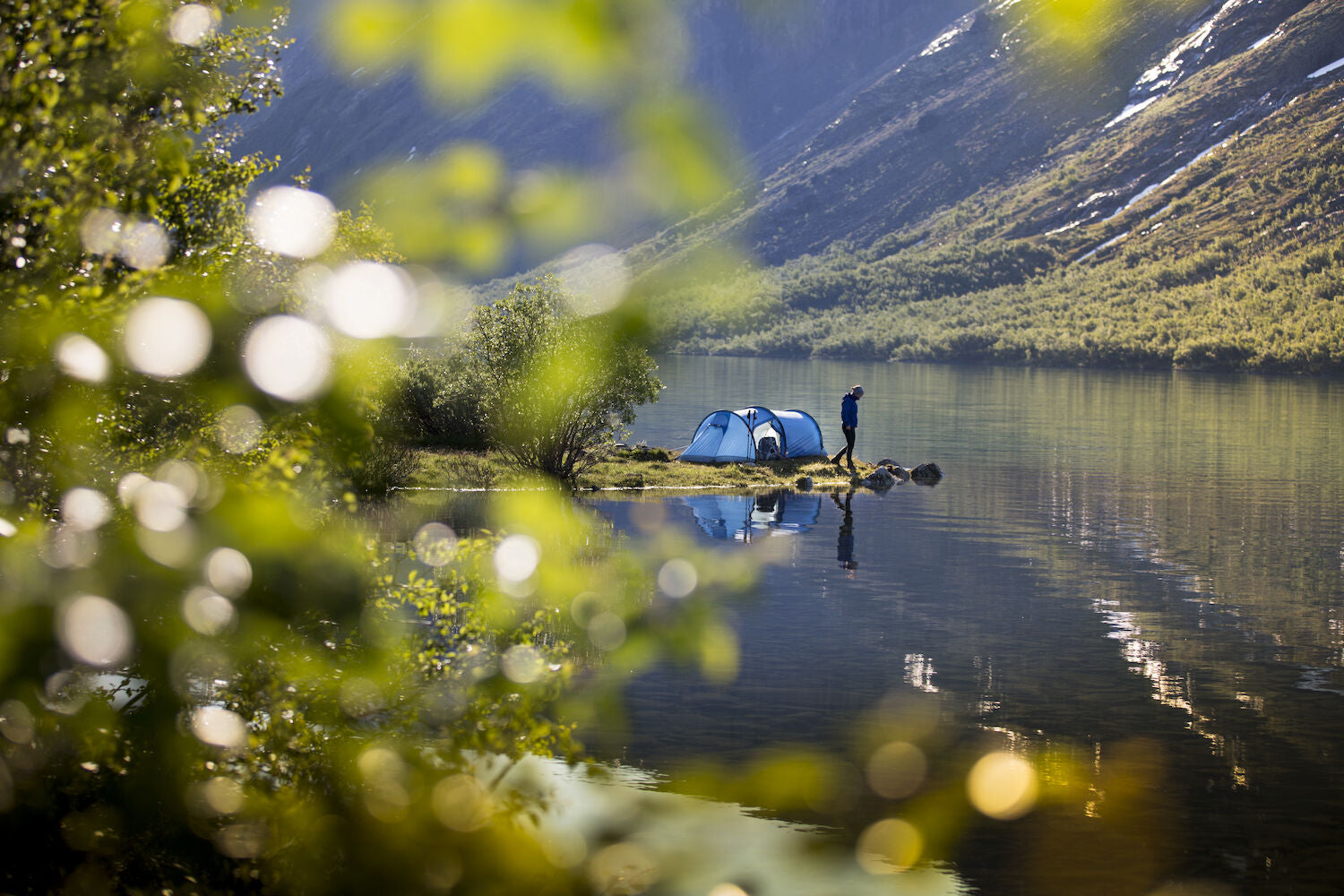 Two tents by a lake with mountains in the background