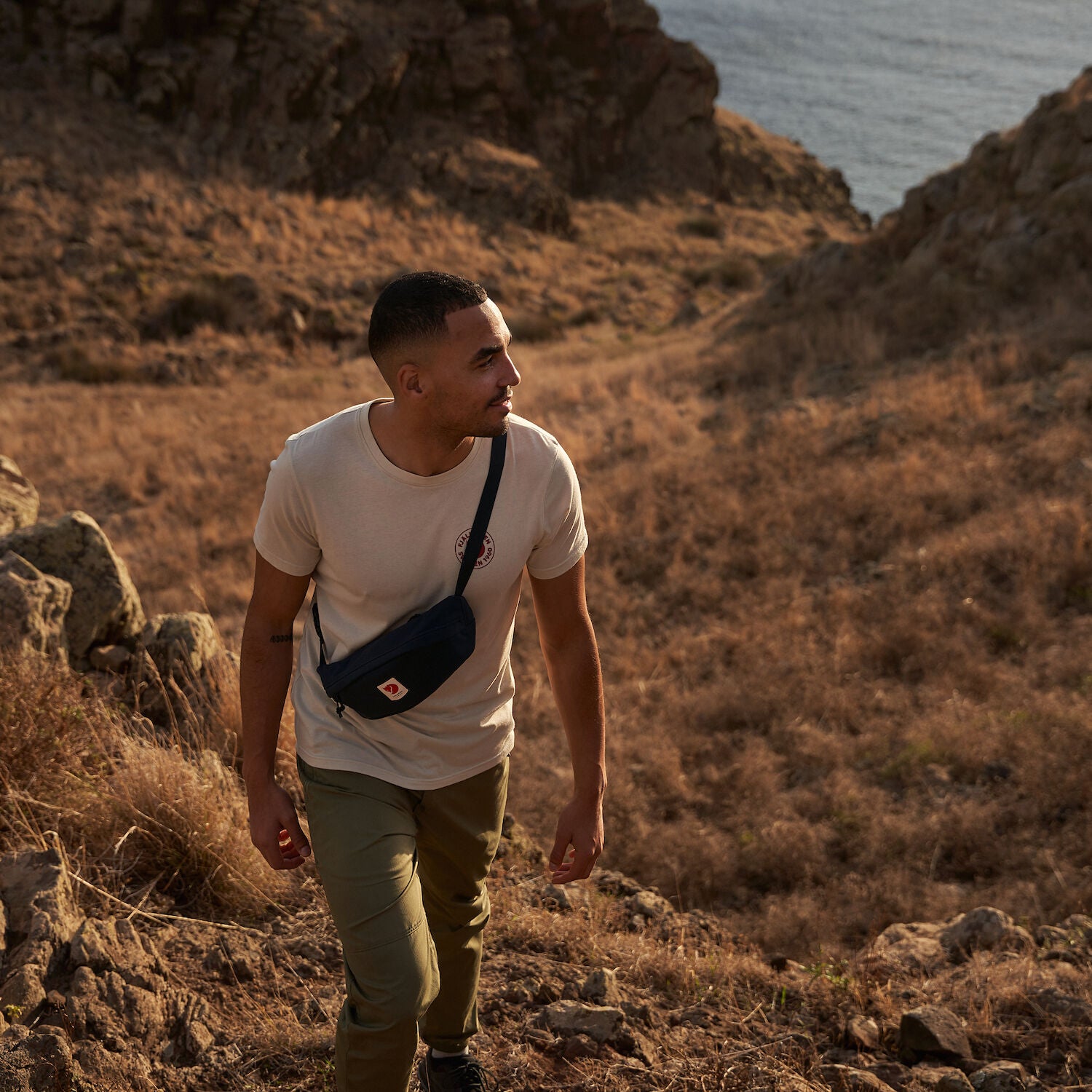 man wearing grey melange round neck t-shirt walking up a grass terrain