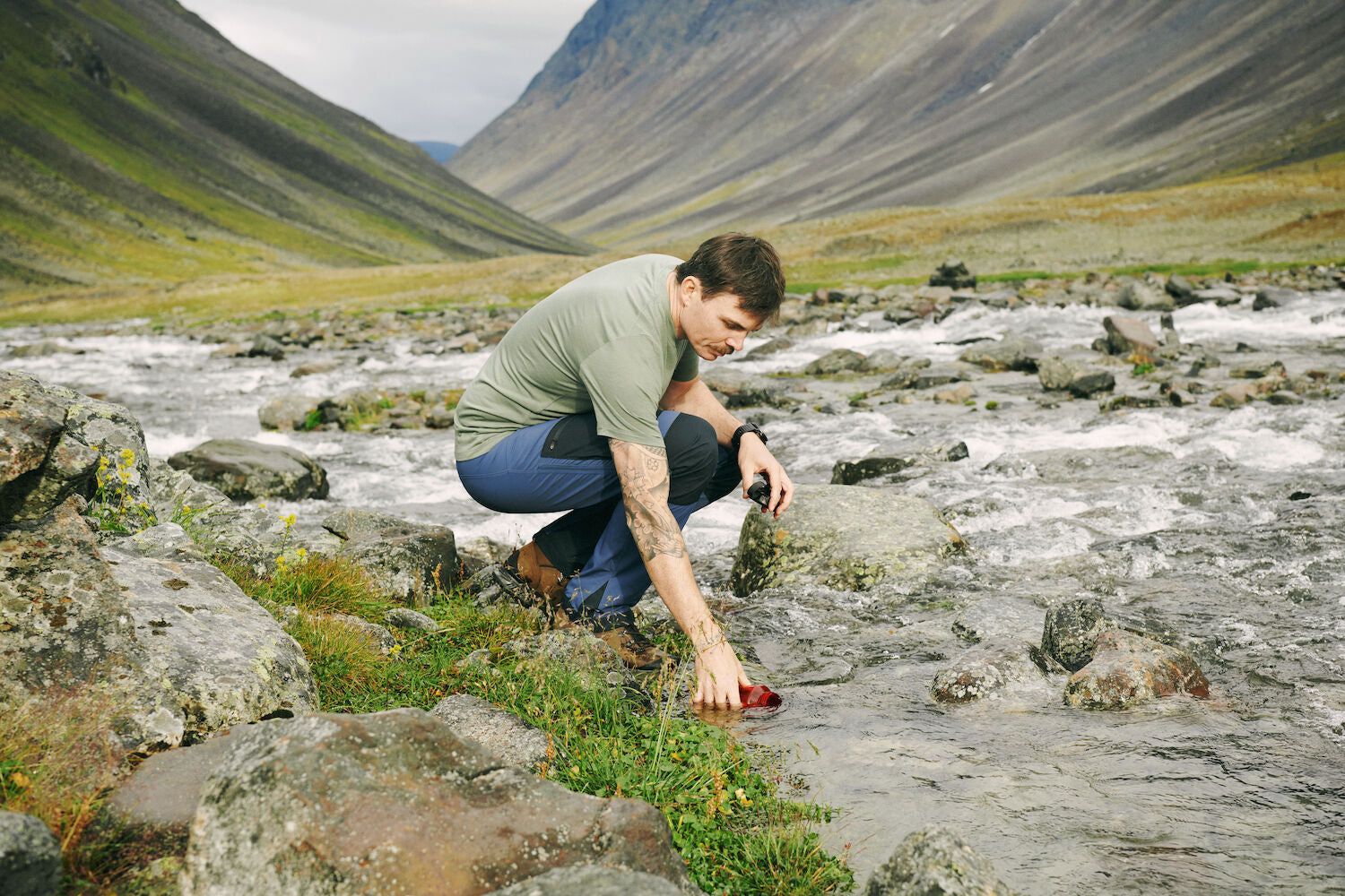 men filling up his bottle along stream river in the mountains