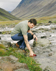 men filling up his bottle along stream river in the mountains