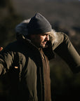 man trying to wear his green parka with fur hood and a grey beanie
