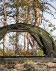 Green camping tent set up in a forested area with trees in the background.