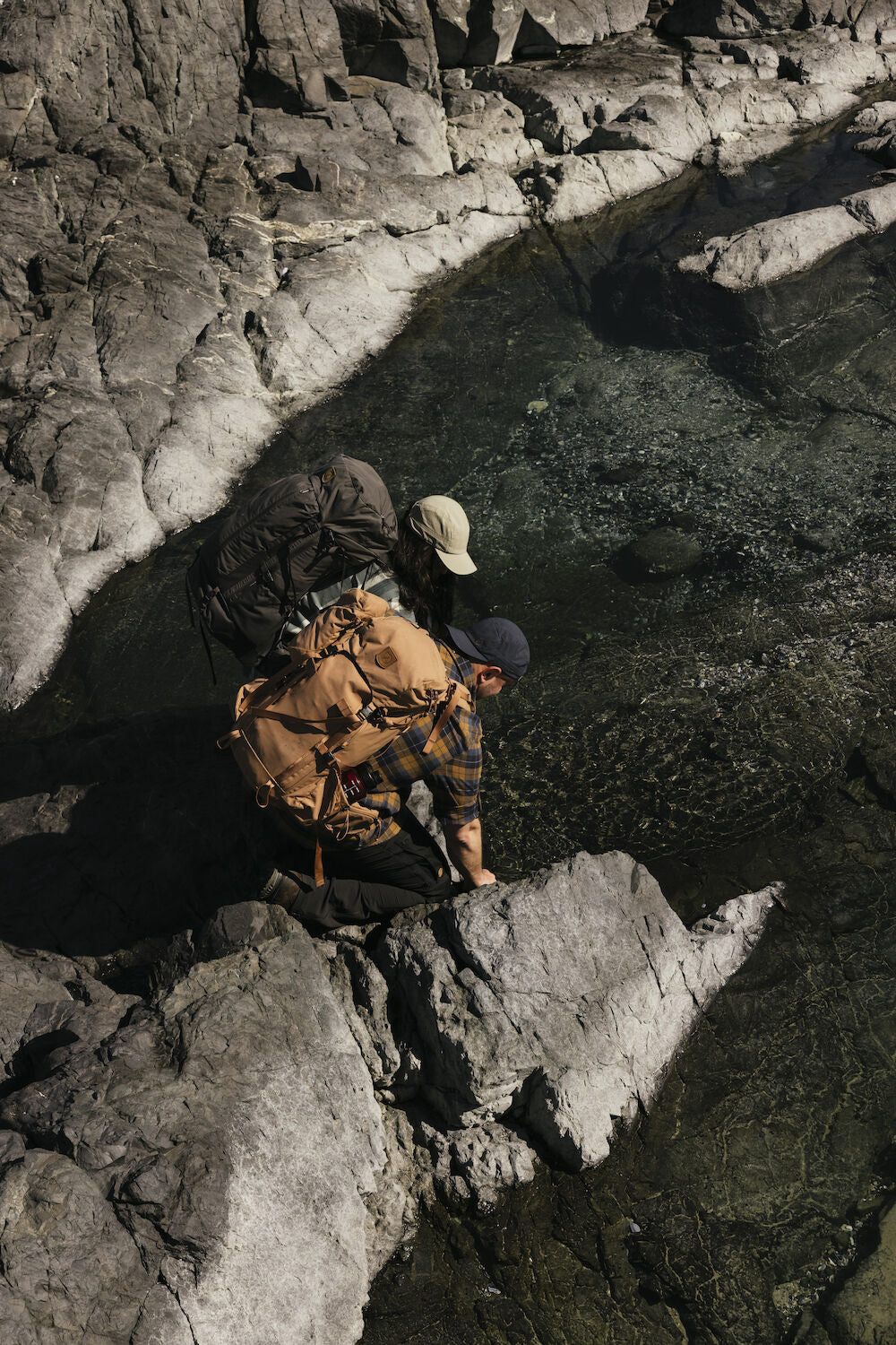 Two people with backpacks standing on rocky terrain near a body of water.