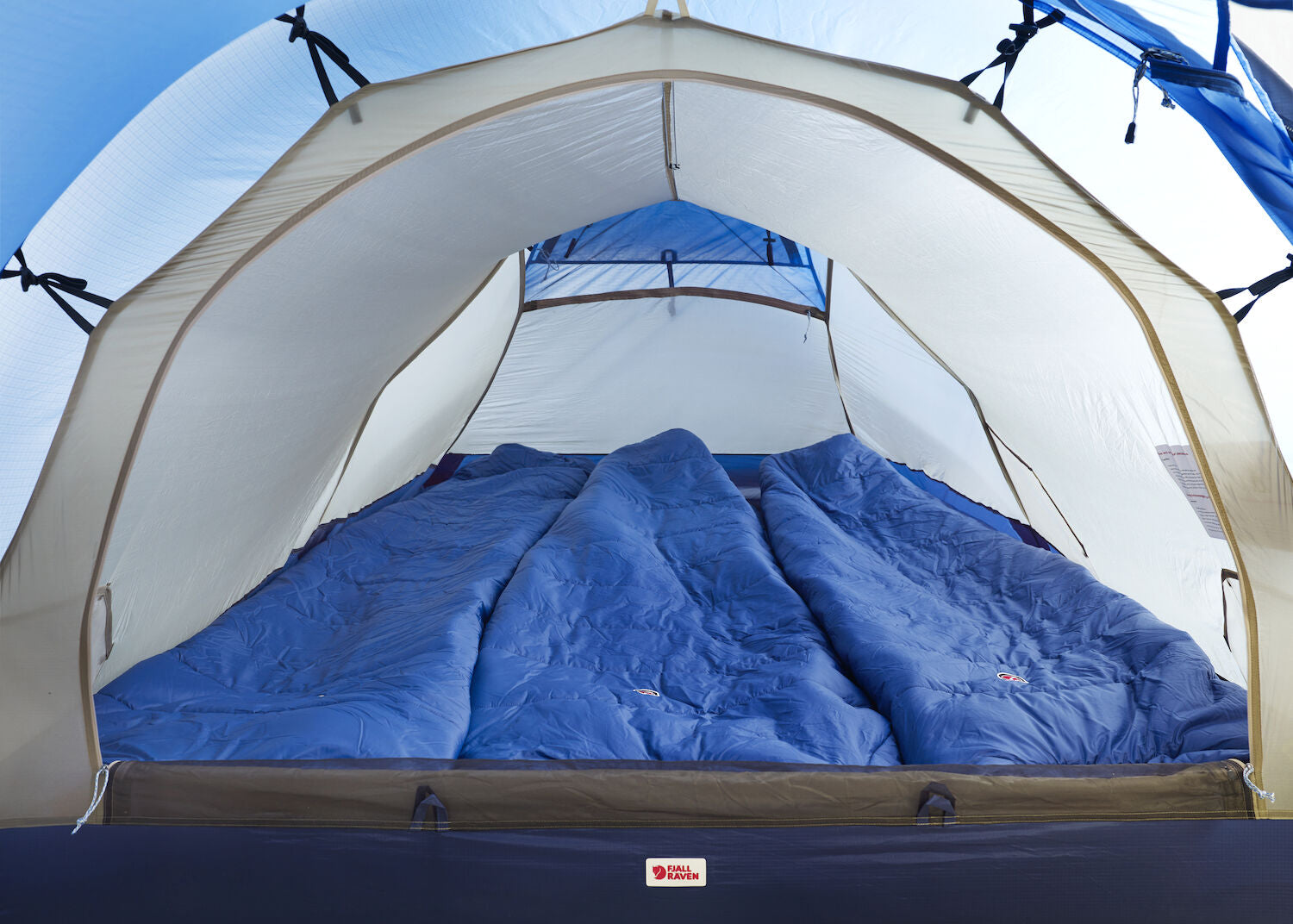 Blue sleeping bags inside a tent with a clear blue sky background