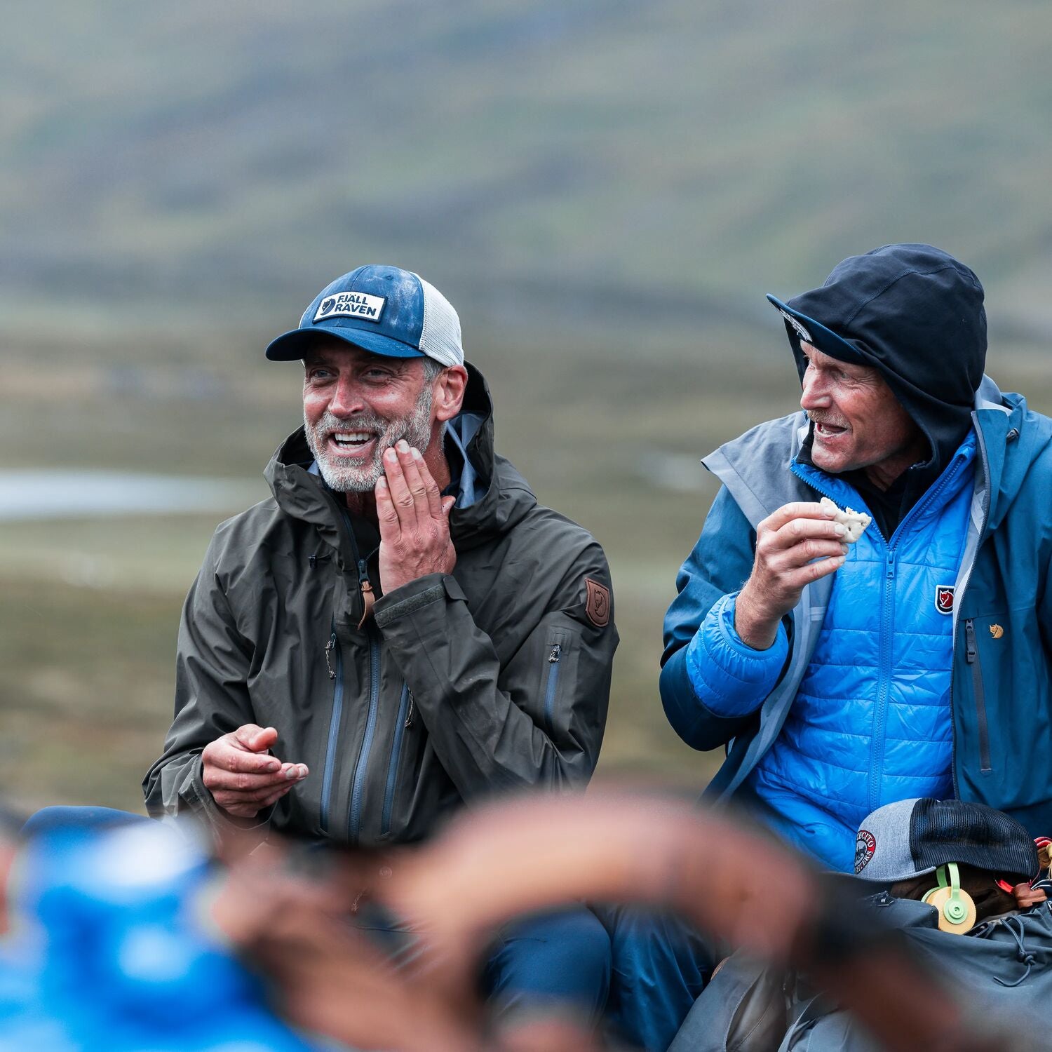 Two men in outdoor clothing sitting together with a scenic background