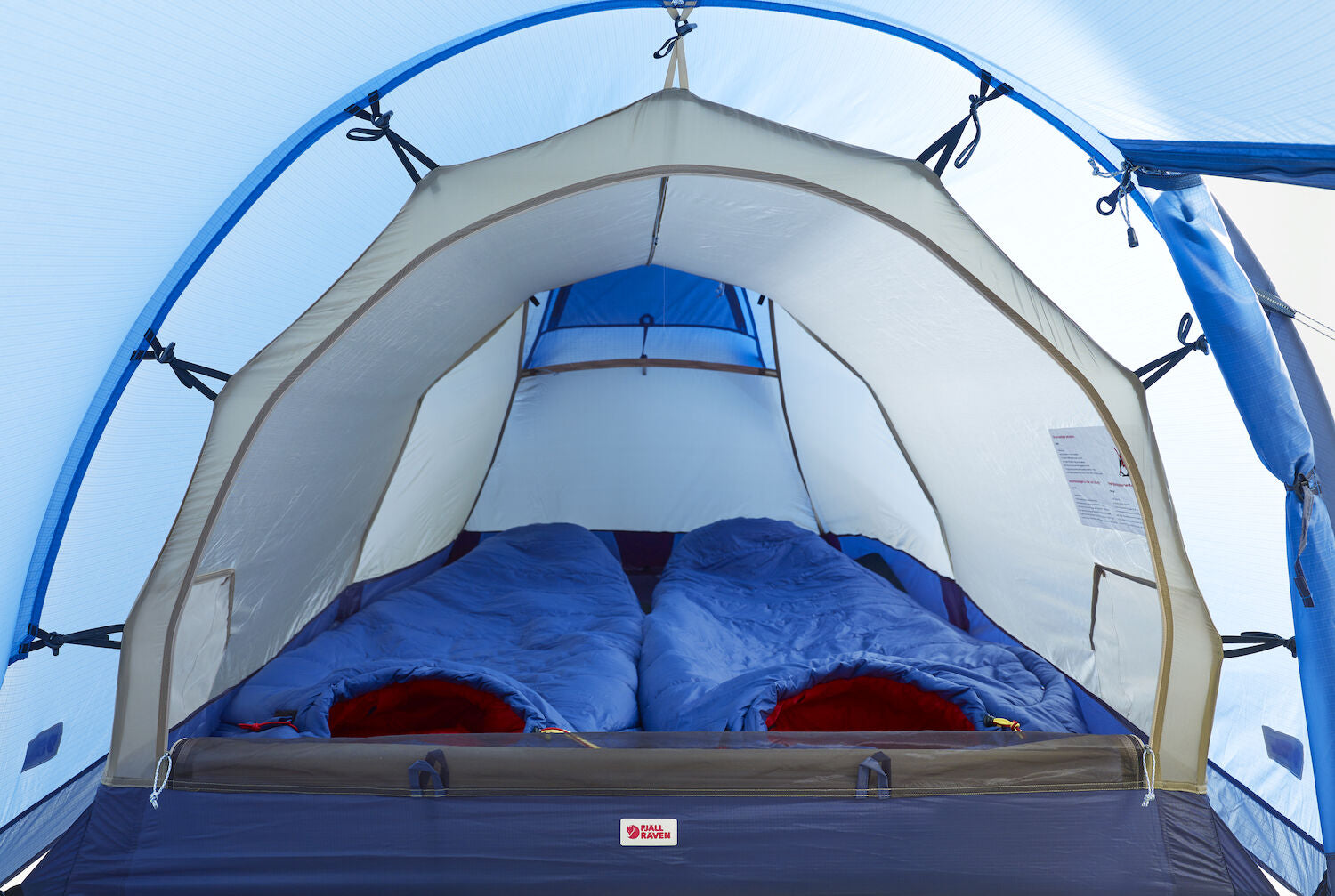 Camping tent with two sleeping bags inside, set against a clear blue sky.