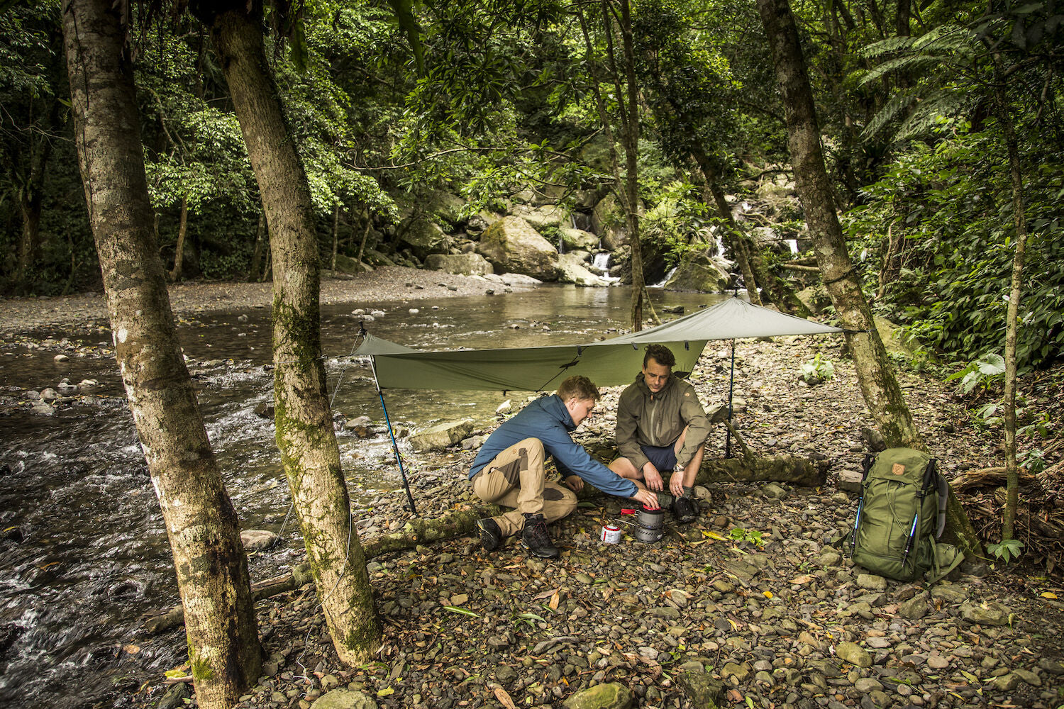 Two people setting up a tent in a forest by a stream