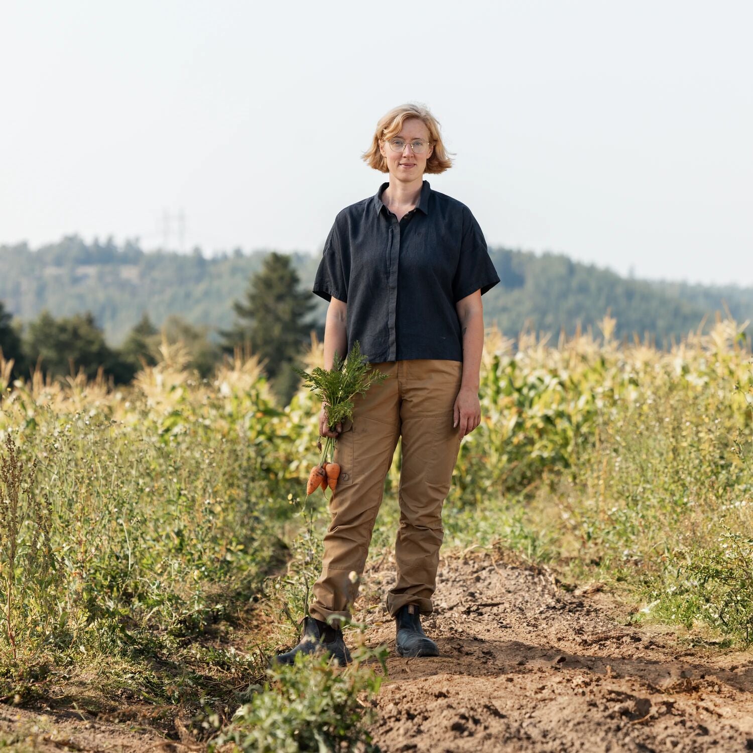 Person standing in a field holding carrots with a natural background
