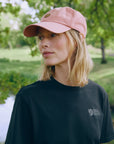 Person wearing a pink cap and black t-shirt with a Fjällräven  logo, standing outdoors.