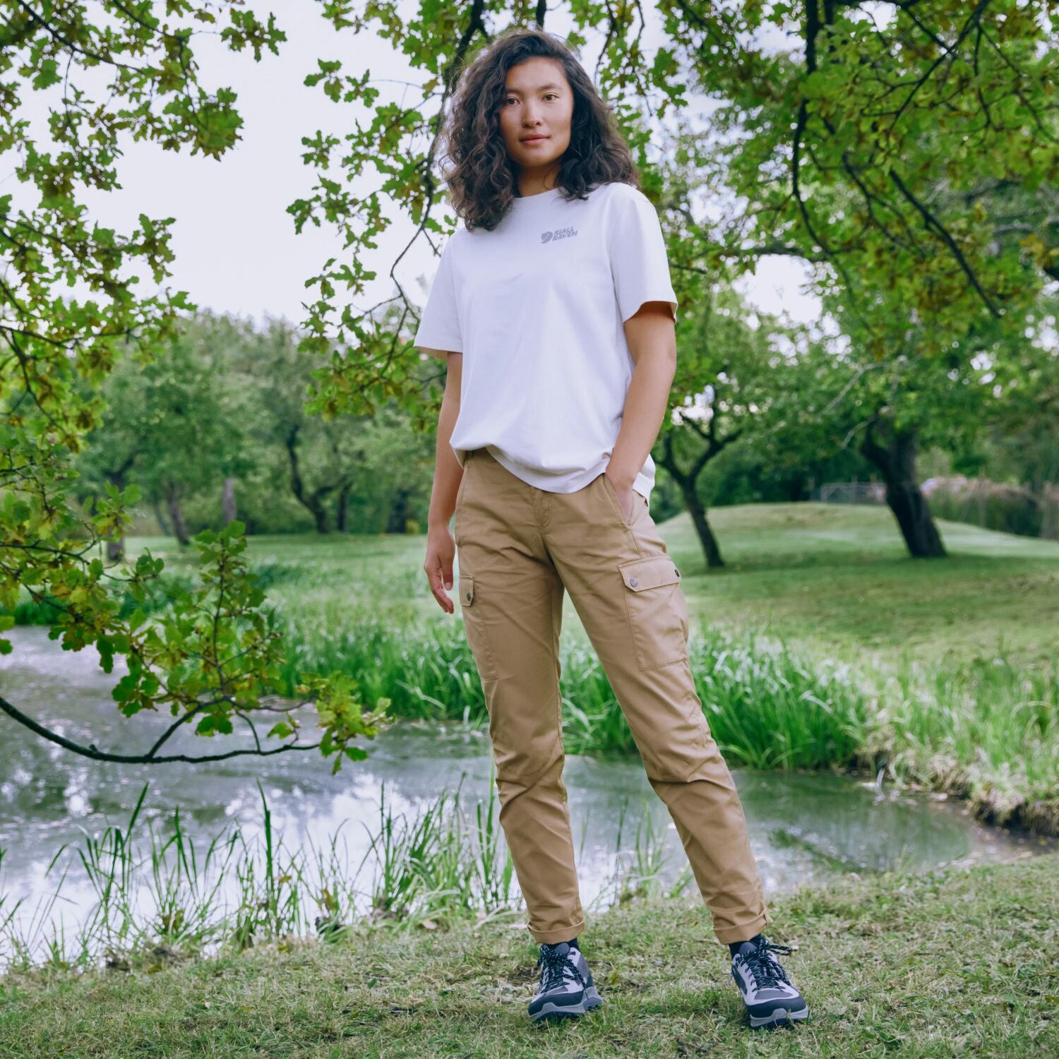 Woman standing in a park with trees and a pond in the background