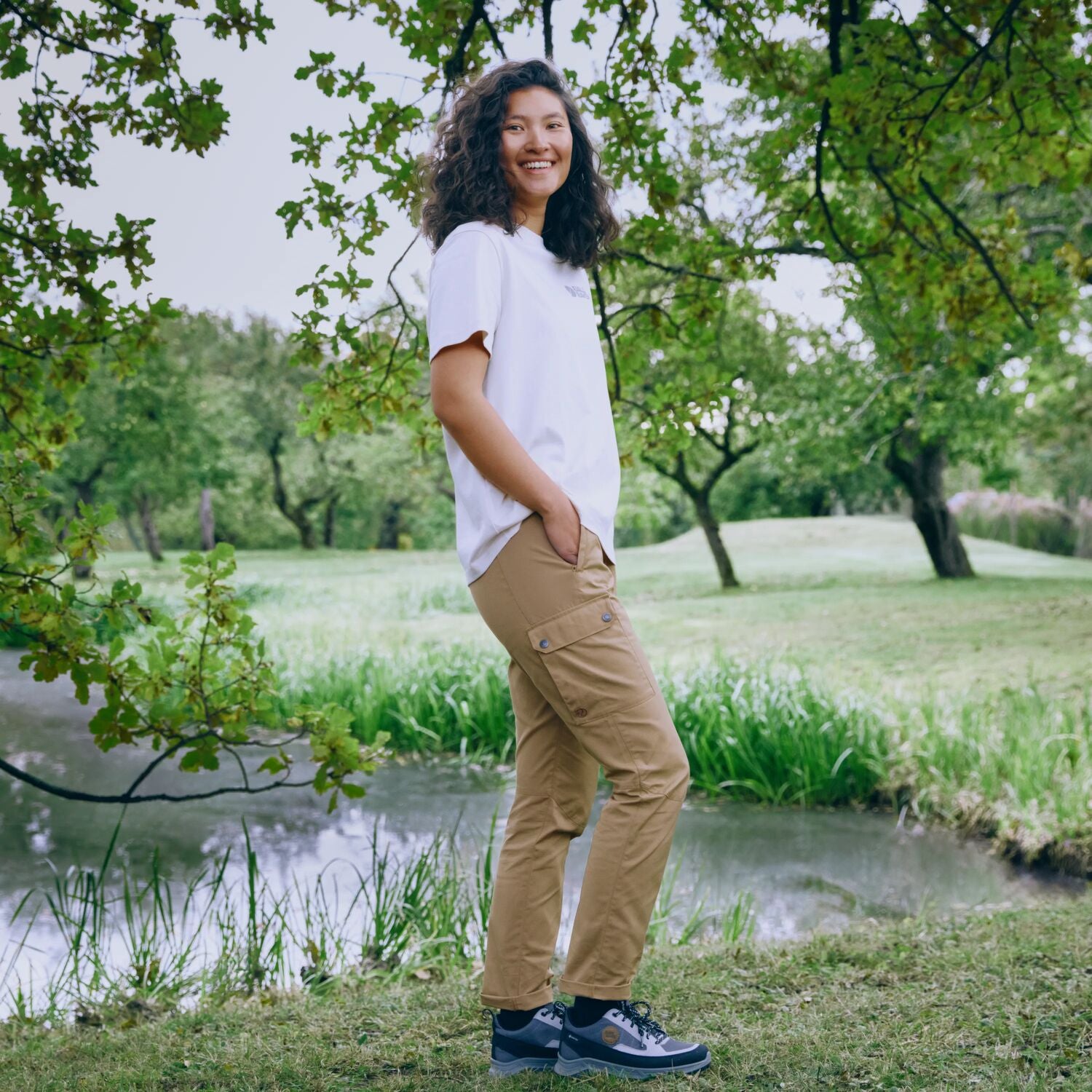 Person standing in a park with trees and a pond in the background