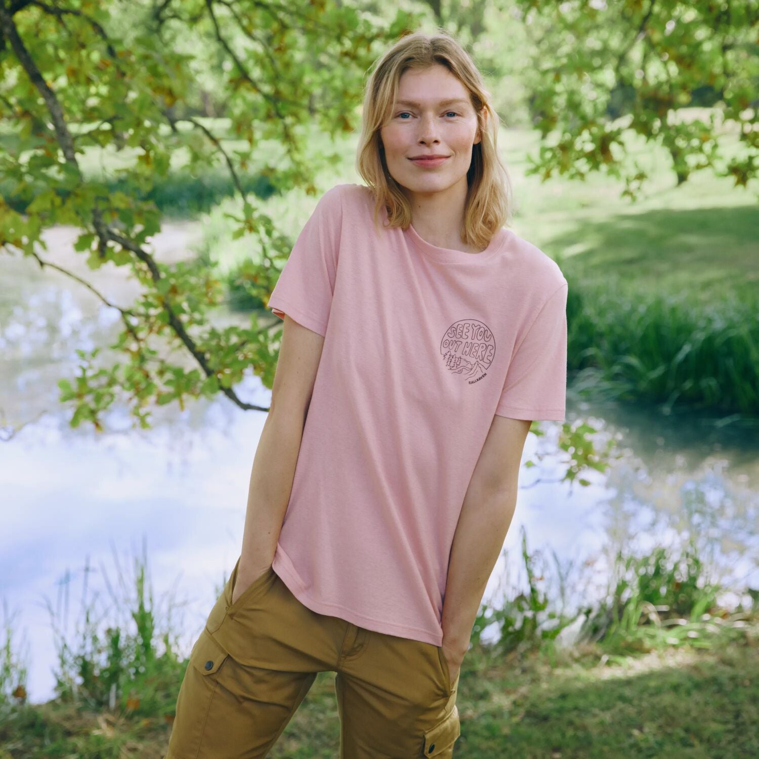 Person wearing a pink t-shirt with a logo in a natural setting
