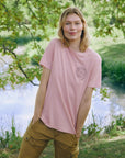 Person wearing a pink t-shirt with a logo in a natural setting