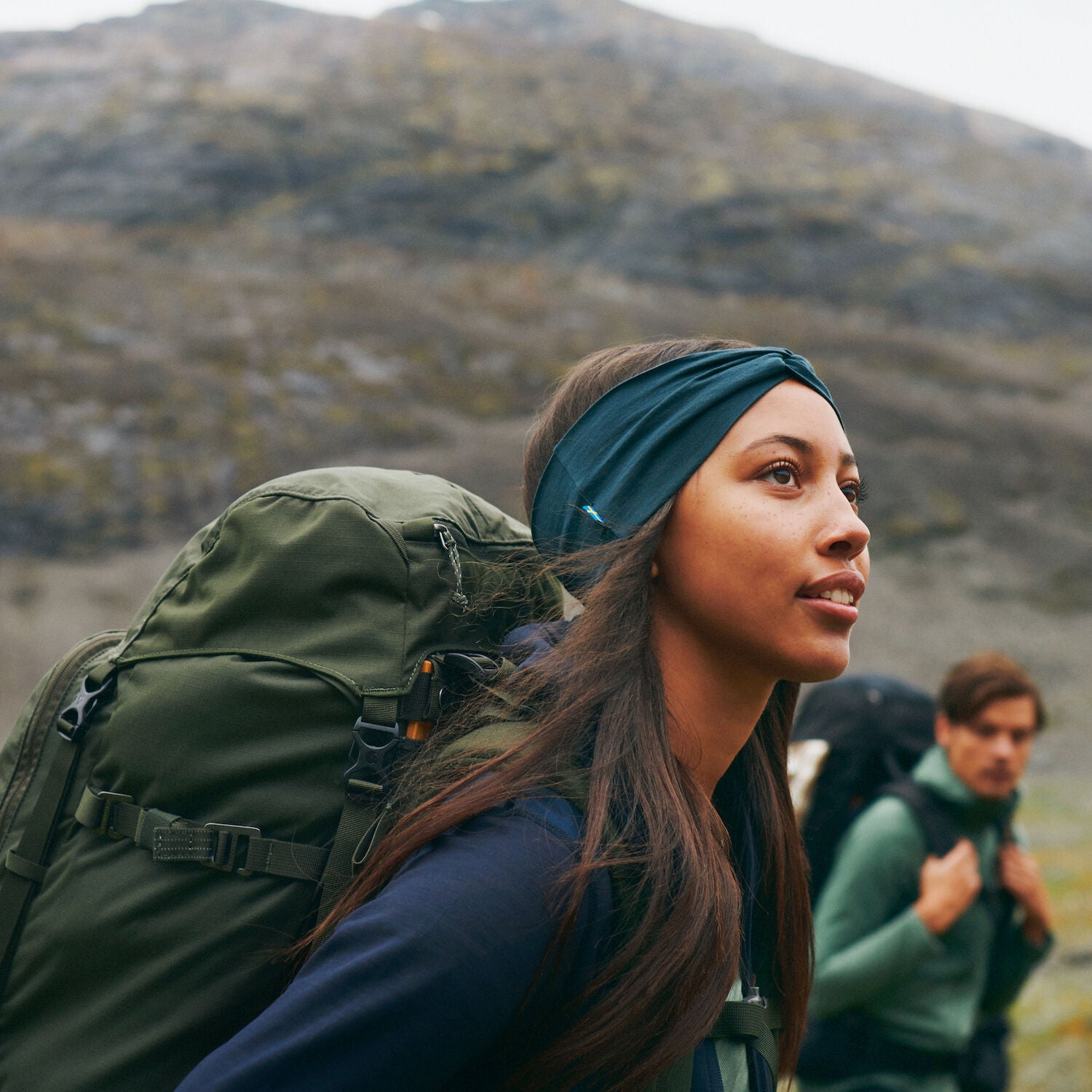 Two people hiking in a mountainous area with green backpacks.