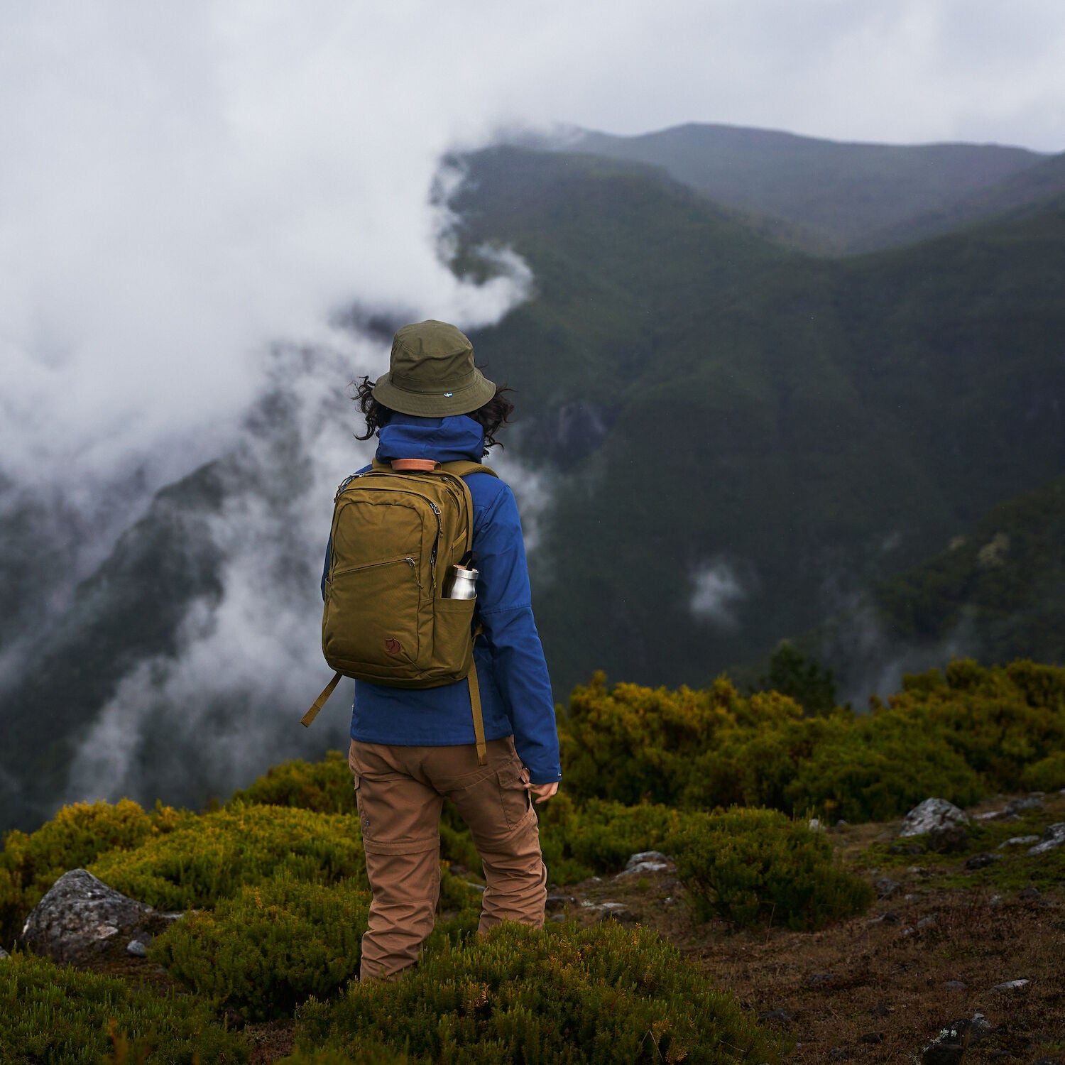 woman wearing indigo blue jacket carrying backpack hiking a mountain