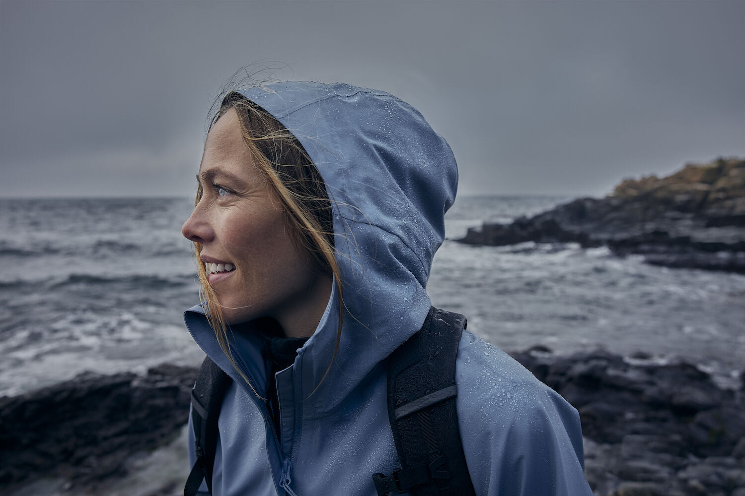 woman in dawn blue windbreaker jacket with hood along rocky coast