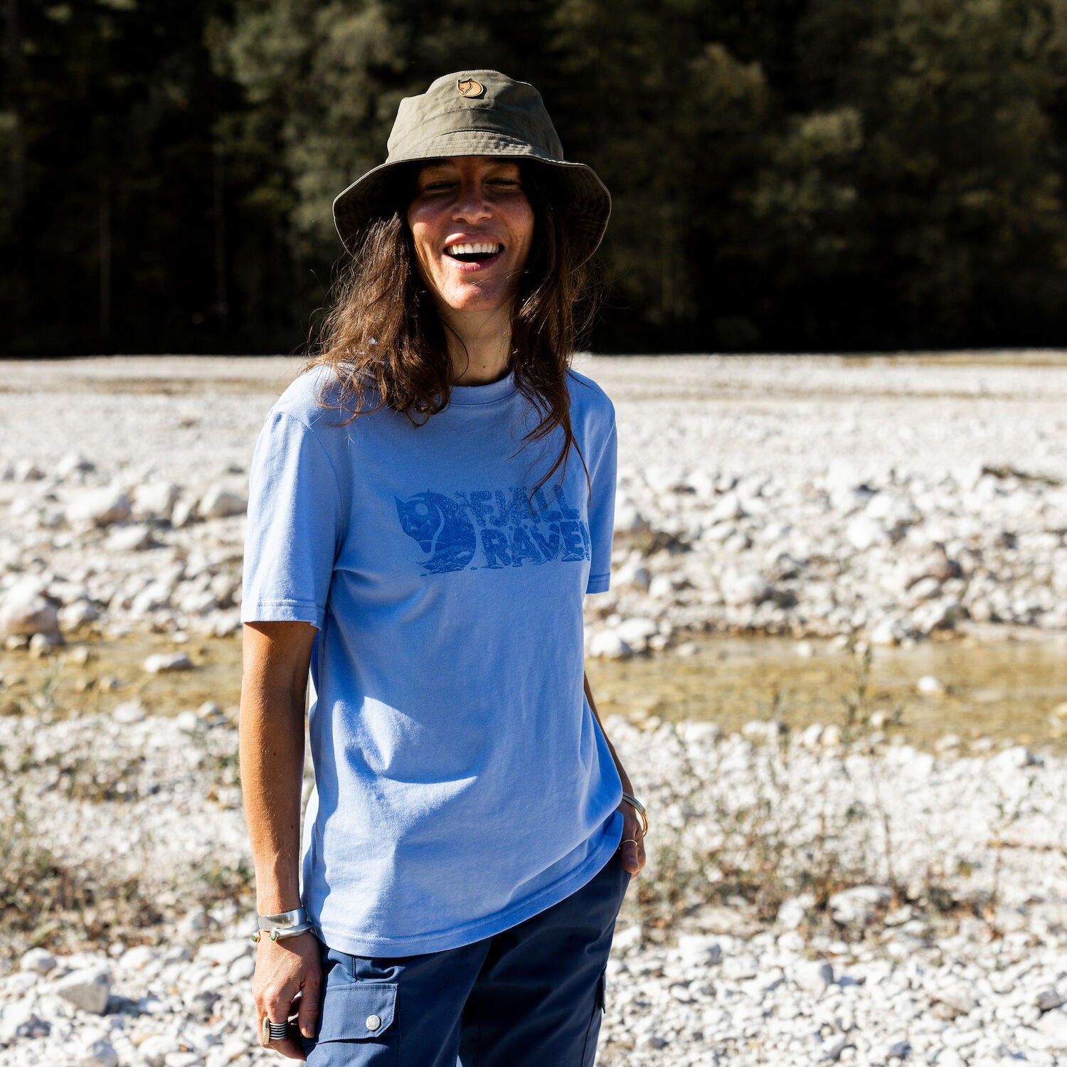 woman wearing blue round neck t-shirt and green bucket hat on rocky surface