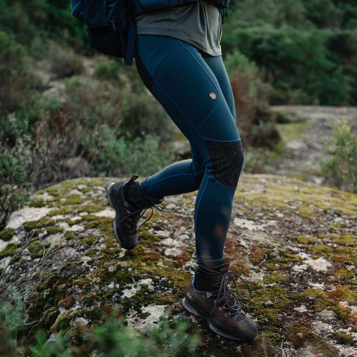 woman wearing blue tights with reinforced knees and Fjällräven logo walking on grass surface