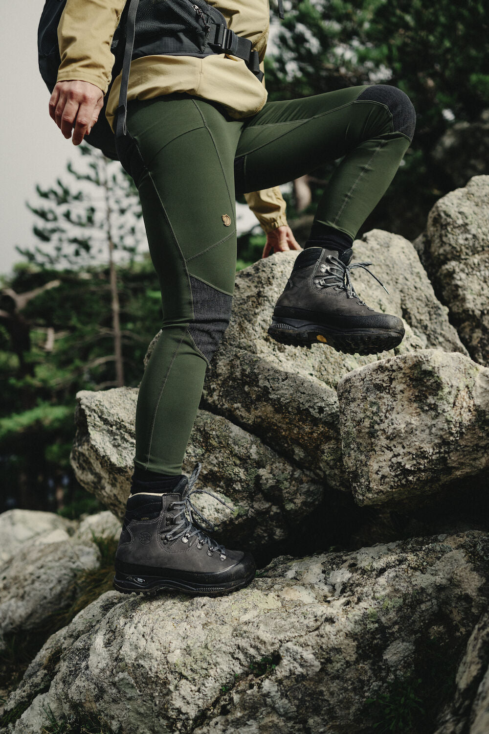 woman wearing deep forest tights with reinforced knees and Fjällräven logo climbing a rocky surface
