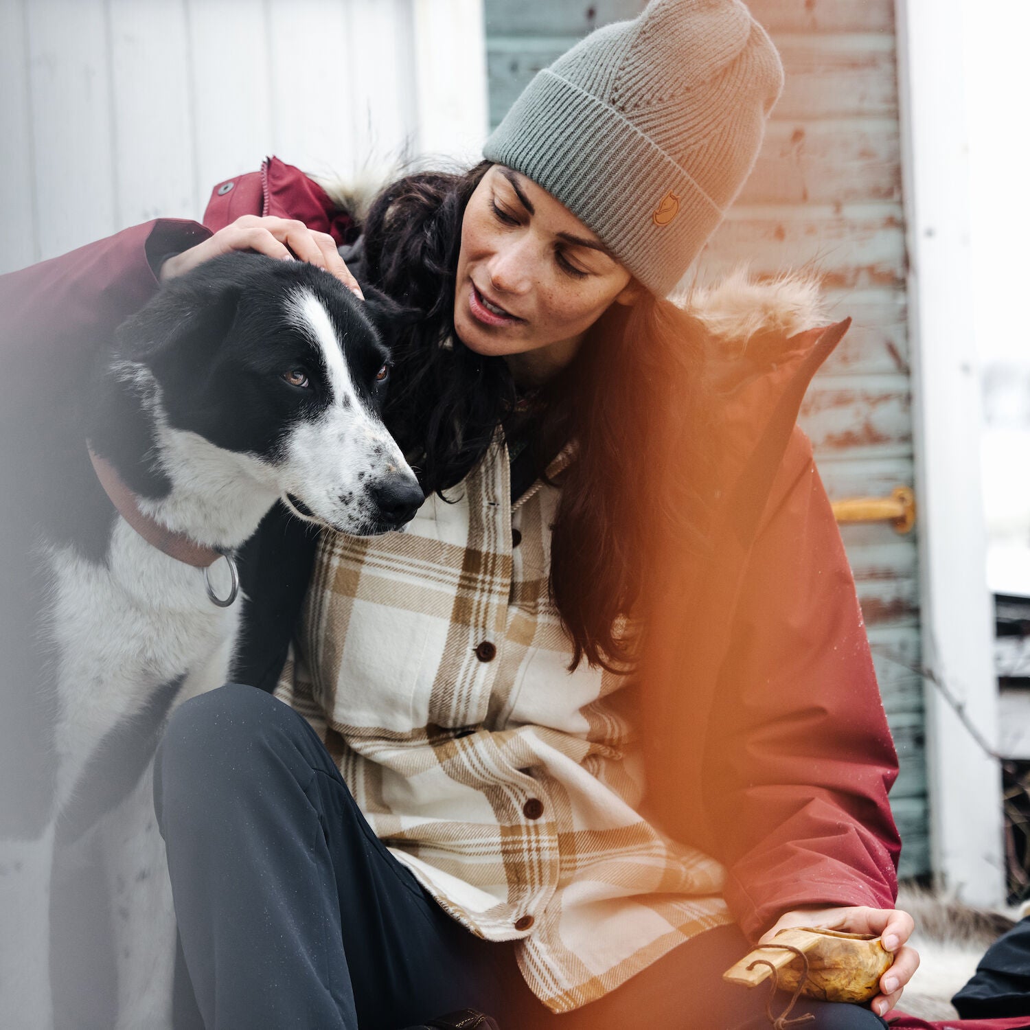 woman in chalk white-dune beige checkered shirt and grey beanie petting a dog