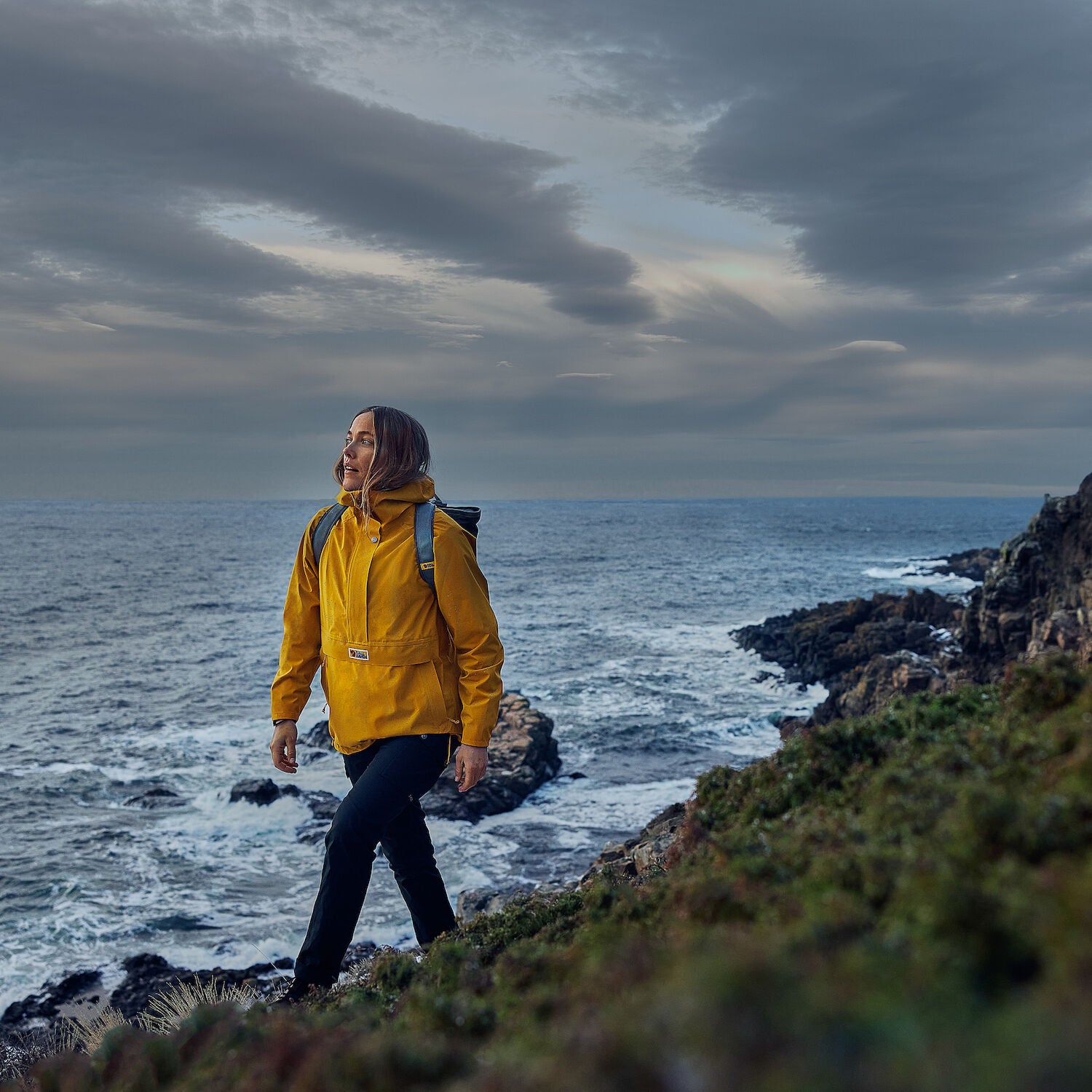 woman wearing yellow waterproof rain jacket with Fjällräven logo walking on the coast