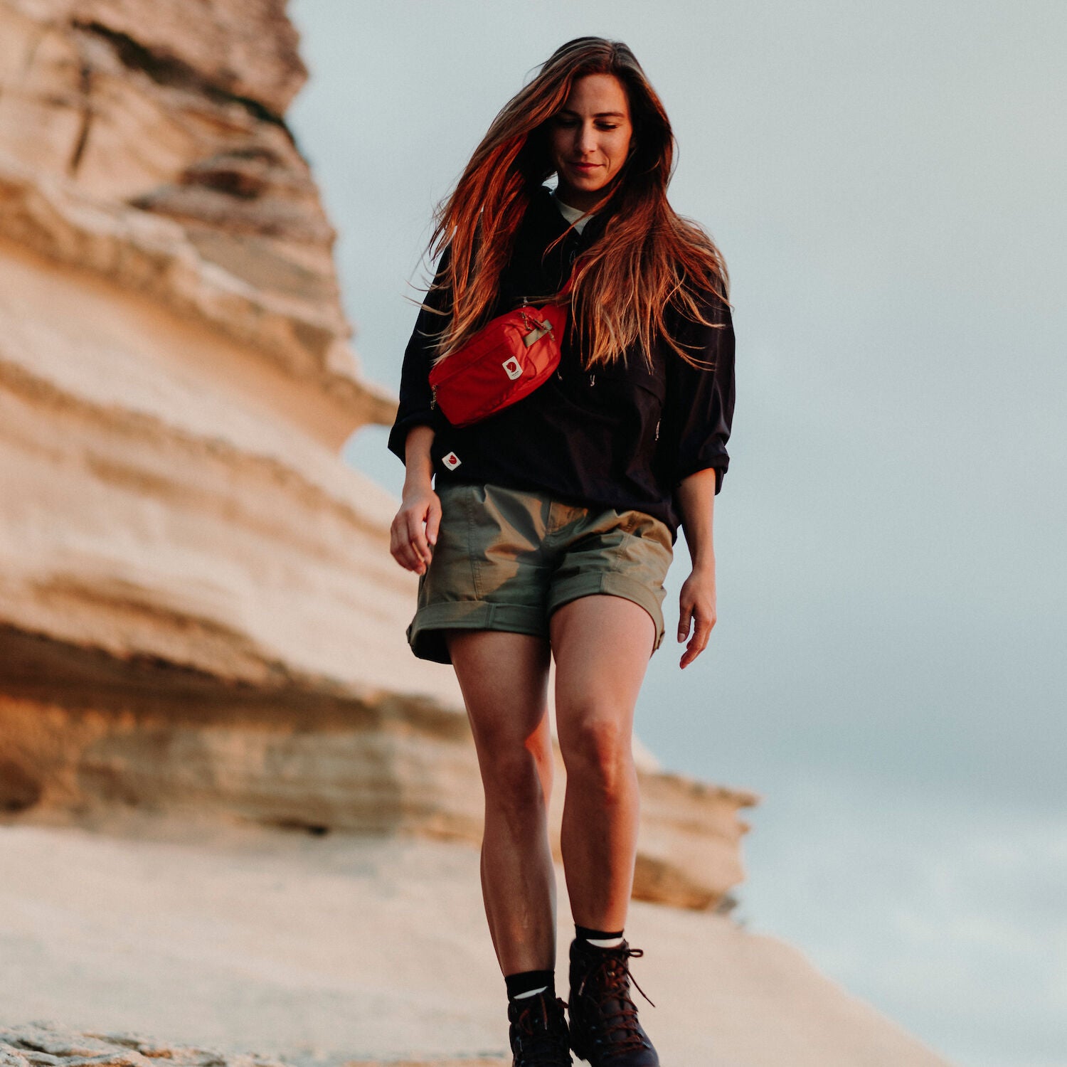 woman wearing black top and beige bermudas shorts carrying a red sling bag