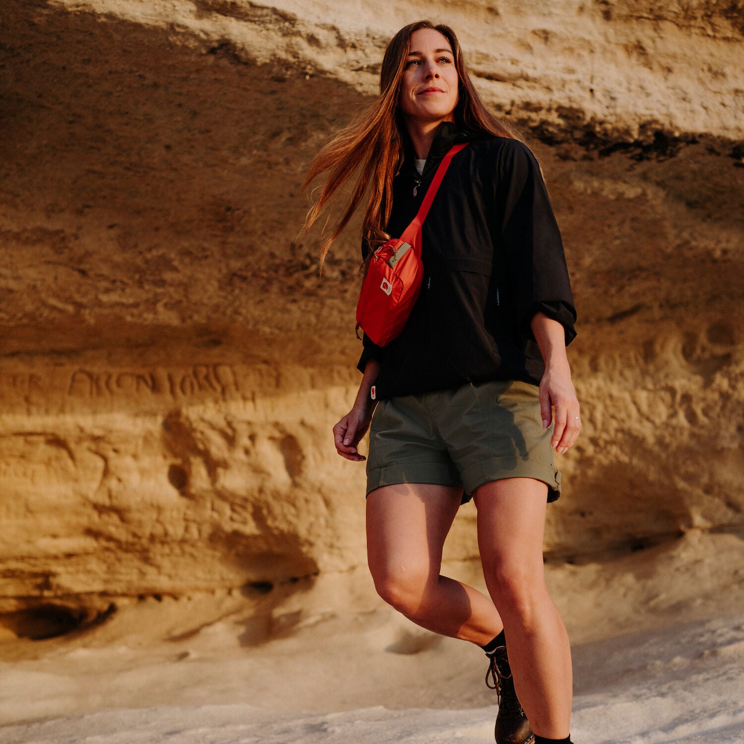 woman wearing black top and green bermudas shorts carrying a red sling bag
