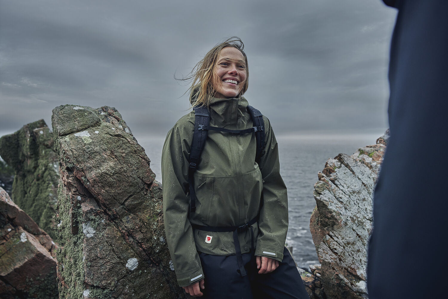 woman in laurel green windbreaker jacket with hood resting on a stone